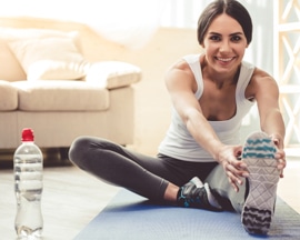 Жена прави упражнения за раздвижване върху килимче за йога, за да се предпази от тежест в краката